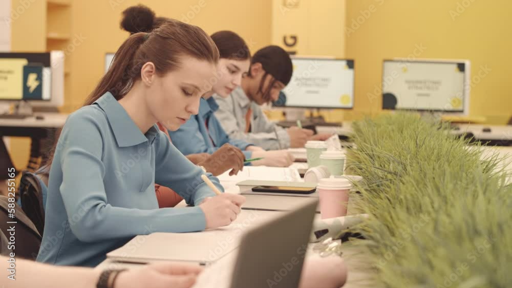 Waist up slowmo of group of multicultural university students studying at desk in bright modern IT class Waist up slowmo of group of multicultural university students studying at desk in bright modern IT class