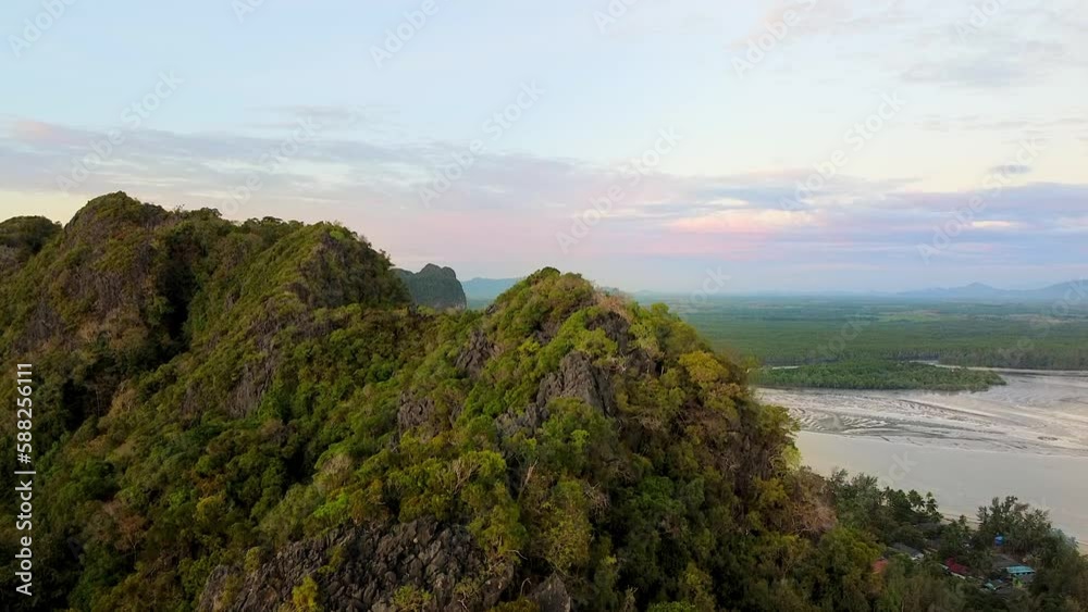 Beautiful aerial of tropical tree covered mountains during red evening dusk scenery. Drone flying upward revealing view of river and beach landscape in distance in Ko Libog Mueang Trang, Thailand. Beautiful aerial of tropical tree covered mountains during red evening dusk scenery. Drone flying upward revealing view of river and beach landscape in distance in Ko Libog Mueang Trang, Thailand.