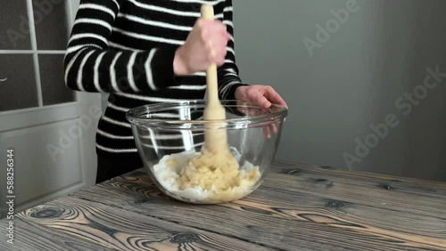 Unrecognizable woman mashing bananas and sugar in a glass bowl while baking banana bread, cooking at home in the kitchen at a wooden table