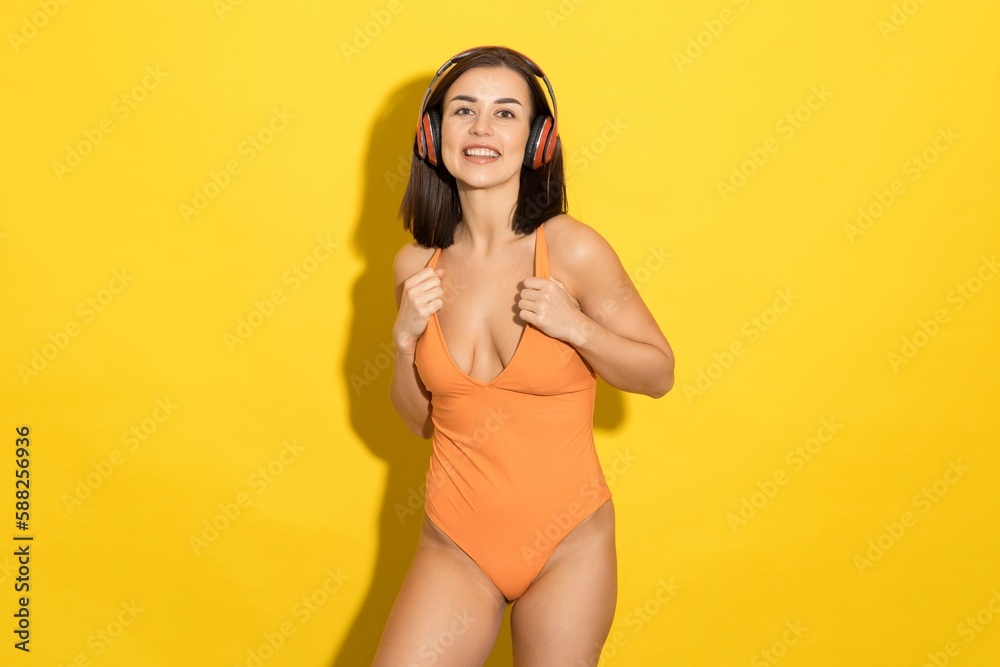 Fototapeta premium The perfect summer day is depicted in this image of a young woman enjoying her music in a swimsuit against a sunny yellow background