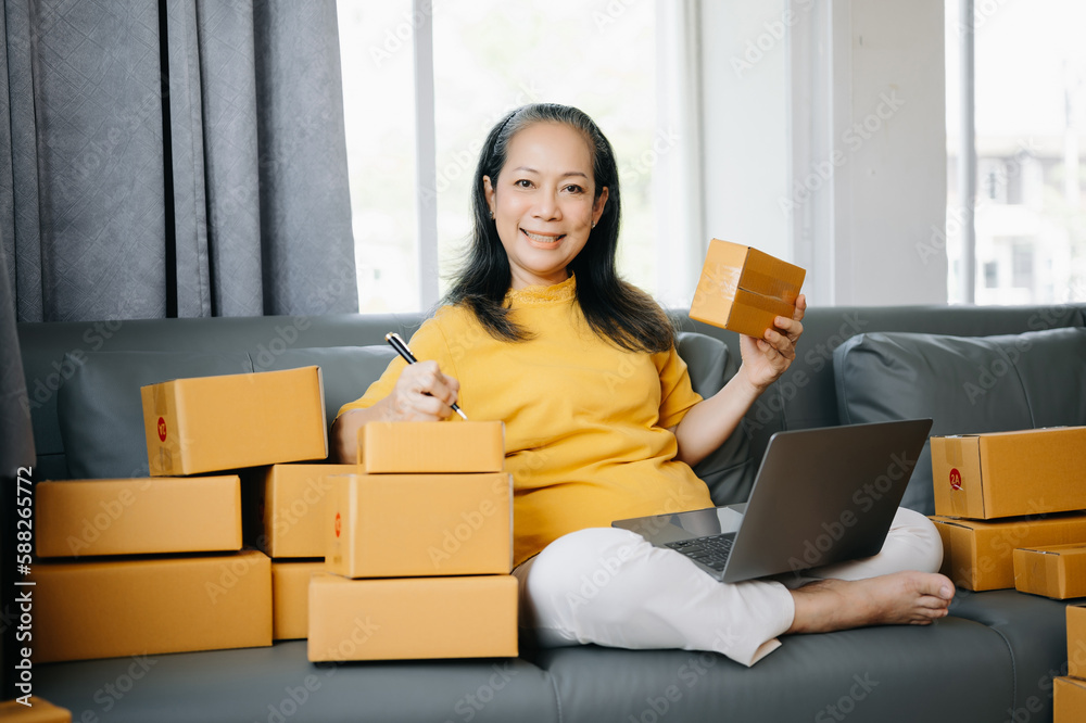 Senior business owner woman prepare parcel box and standing check online orders for deliver to customer on tablet, laptop Shopping Online concept.. Senior business owner woman prepare parcel box and standing check online orders for deliver to customer on tablet, laptop Shopping Online concept..