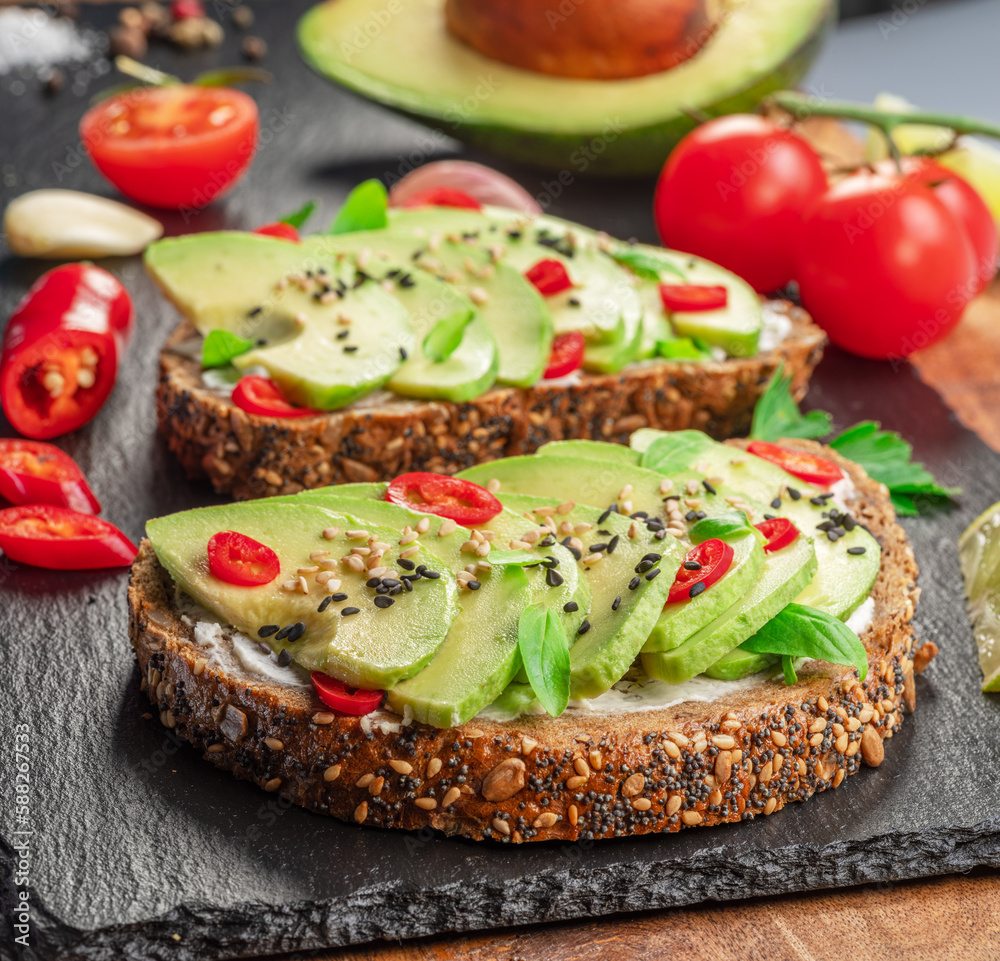 Avocado toasts - bread with avocado slices, pieces of red pepper and sesame  on black stone board.