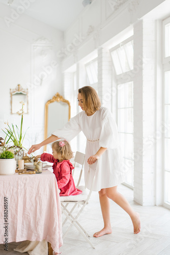 Mom and little daughter are sitting at a festive Easter table in the living room