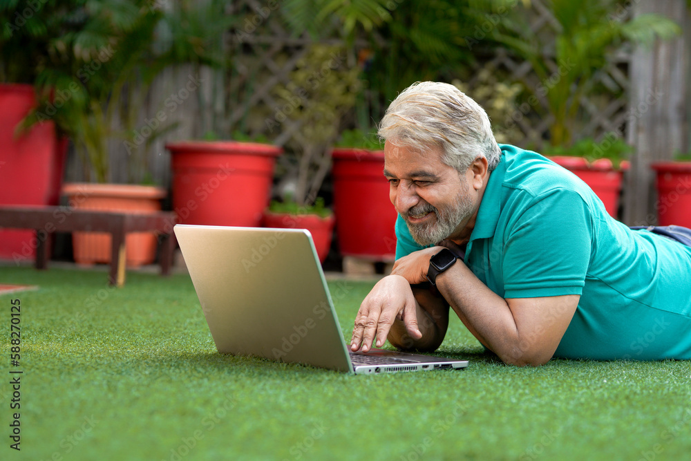 Indian senior man laying down at ground and using laptop. Indian senior man laying down at ground and using laptop.