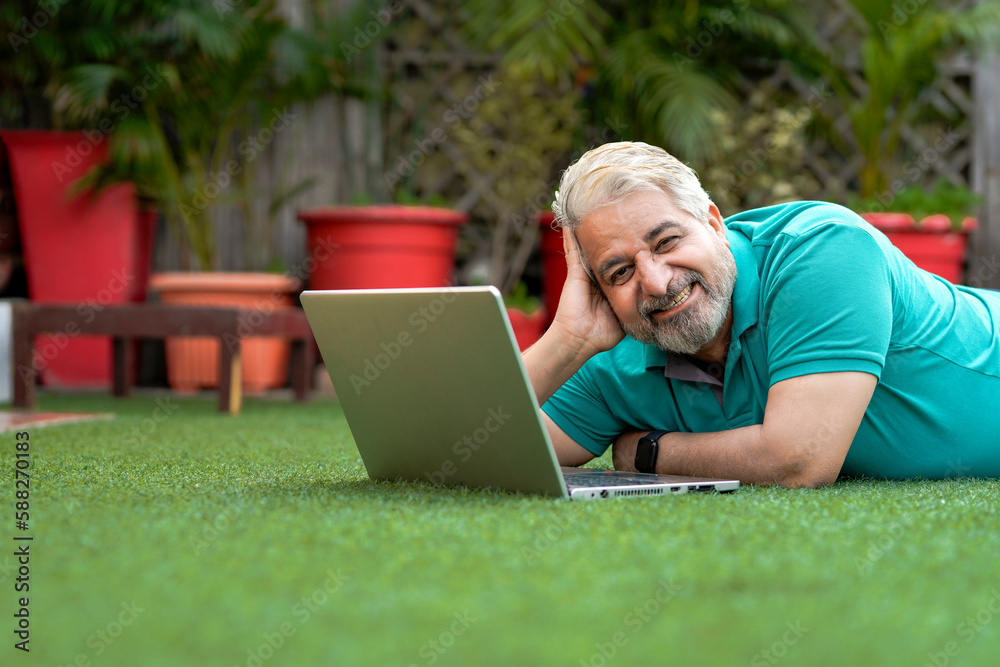 Indian senior man laying down at ground and using laptop. Indian senior man laying down at ground and using laptop.