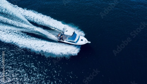 Aerial view of a white speedboat floating in blue water with white foam trails © James Charsley/Wirestock Creators