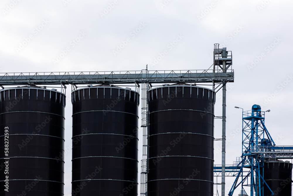 Obraz premium A huge, blackm steel grain silo standing in a field. Warehouses full of grain before the new season