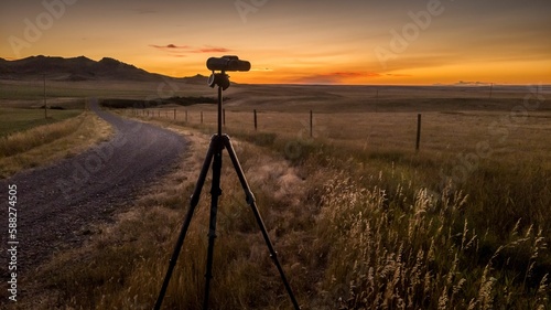 Tripod with a camera in the field a dusty path near and purple sky in the background