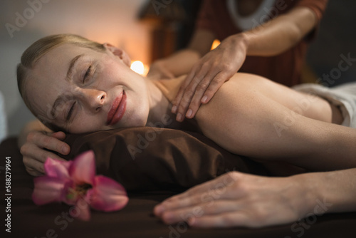 Beautiful caucasian woman having shoulder massage at night spa salon
