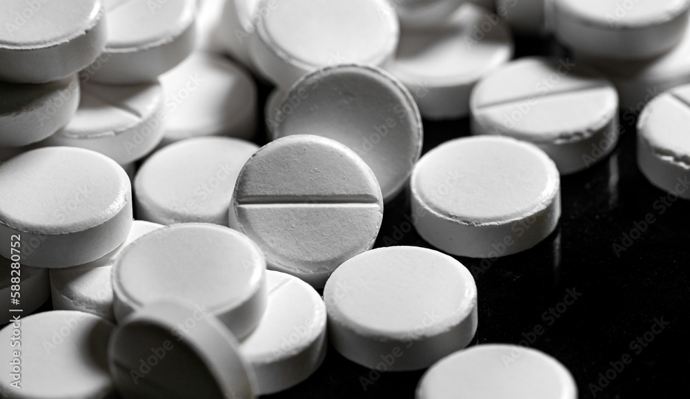 Close up of white painkiller tablet on a reflective black backgr Close up of white painkiller tablet on a reflective black backgr