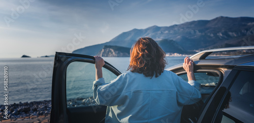 Obraz na płótnie Young happy woman traveler enjoying the sunset at the sea while standing next to the car. Summer holidays and travel concept w salonie