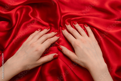 A woman s hand with red nails is trying to rip off a red silk fabric.