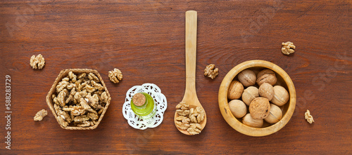Tasty healthy organic walnut vegetable oil in glass bottle, nuts in wooden bowl and shell less nuts in wicker plate and in spoon on wooden brown table. Close-up, flat lay, copy space, banner, mockup photo