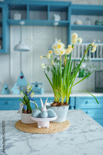 Blue kitchen interior with furniture. Stylish cuisine with flowers in vase. Wooden kitchen in spring decor. Cozy home decor. Kitchen utensils, dishes and plate on table. kitchen island in dining room,