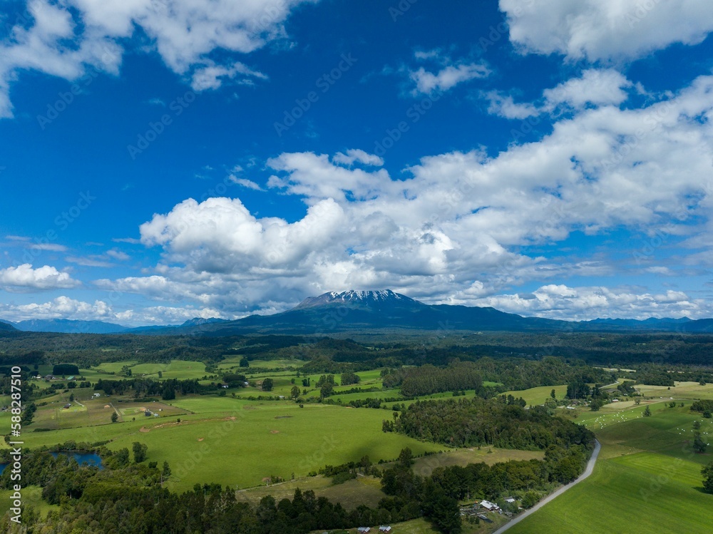 Fototapeta premium Drone shot of the Calbuco Volcano under the blue cloudy sky in Chile with fields on its foot