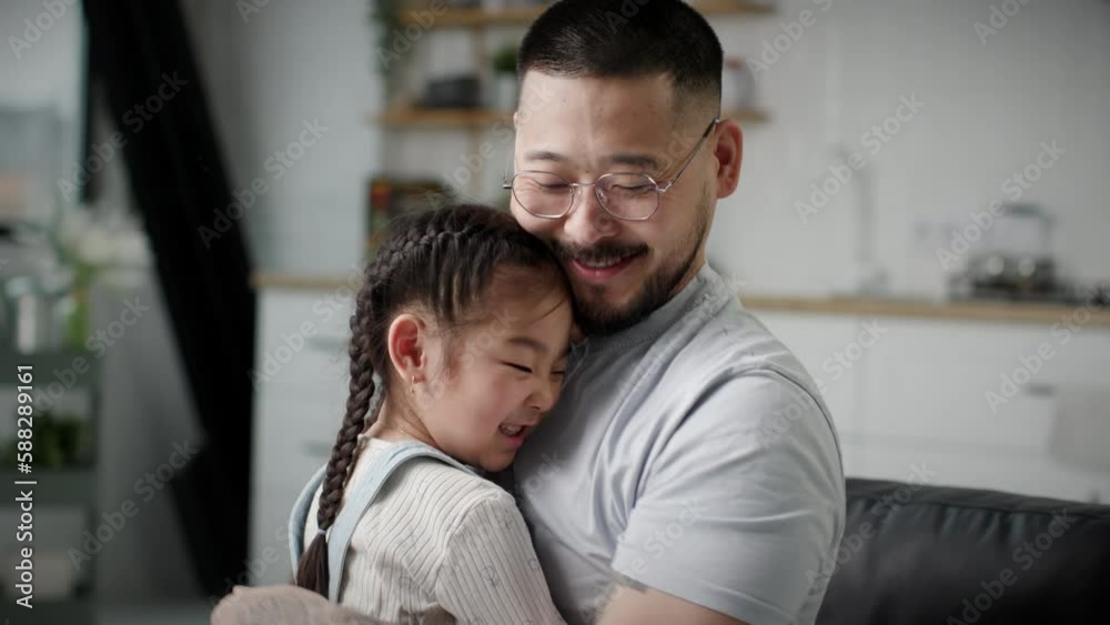 Loving Dad Hugging His Daughter. Happy Asian father and girl hug and kiss sitting at home. Loving Dad Hugging His Daughter. Happy Asian father and girl hug and kiss sitting at home.