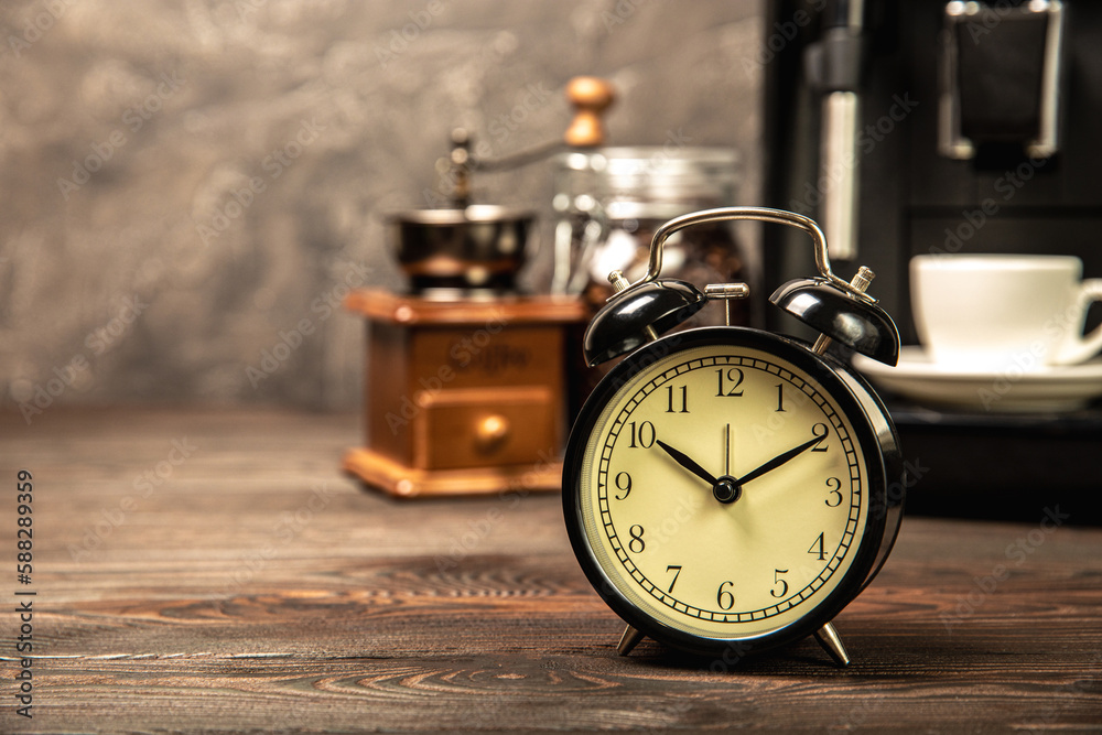 Alarm clock and a cup of morning coffee with a coffee machine on the background of the kitchen interior.A glass of coffee on the table with a clock in the morning. Good morning concept. WAKE UP! Alarm clock and a cup of morning coffee with a coffee machine on the background of the kitchen interior.A glass of coffee on the table with a clock in the morning. Good morning concept. WAKE UP!