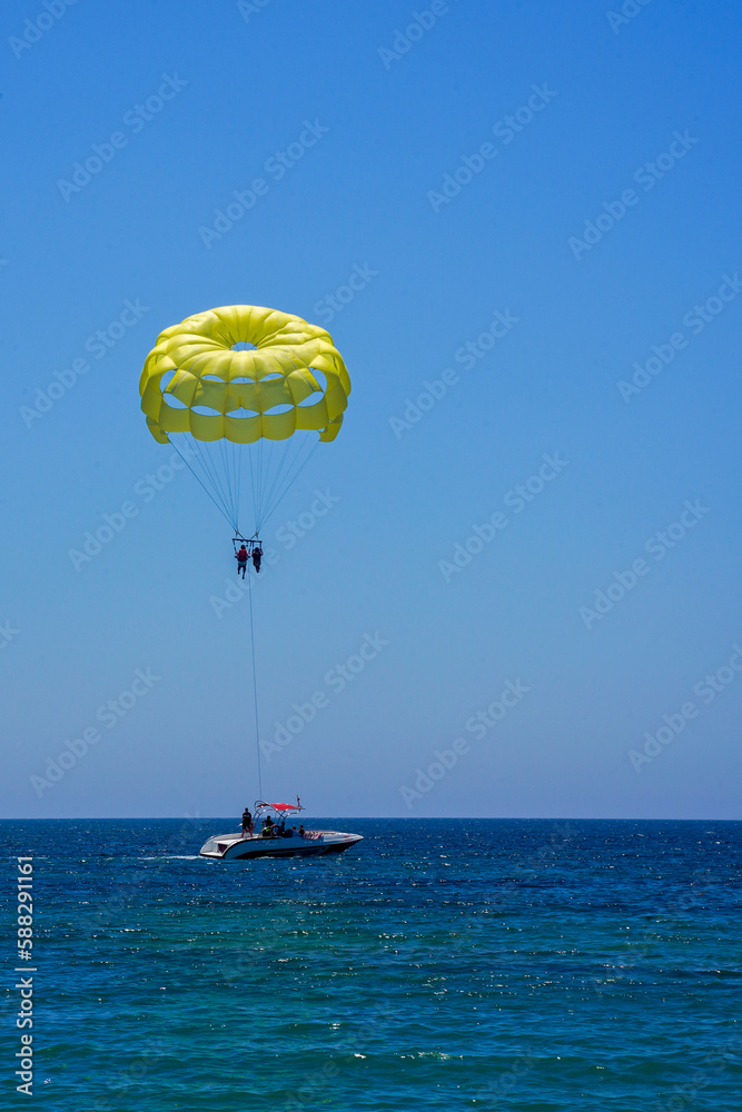 Parasailing on a yellow parachute against the blue sky. Beach extreme adventures. Background vacation, photo for postcards, tourist and travel guide. The concept of summer holidays, vacation, tourism Parasailing on a yellow parachute against the blue sky. Beach extreme adventures. Background vacation, photo for postcards, tourist and travel guide. The concept of summer holidays, vacation, tourism