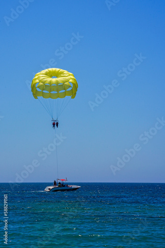 Parasailing on a yellow parachute against the blue sky. Beach extreme adventures. Background vacation, photo for postcards, tourist and travel guide. The concept of summer holidays, vacation, tourism