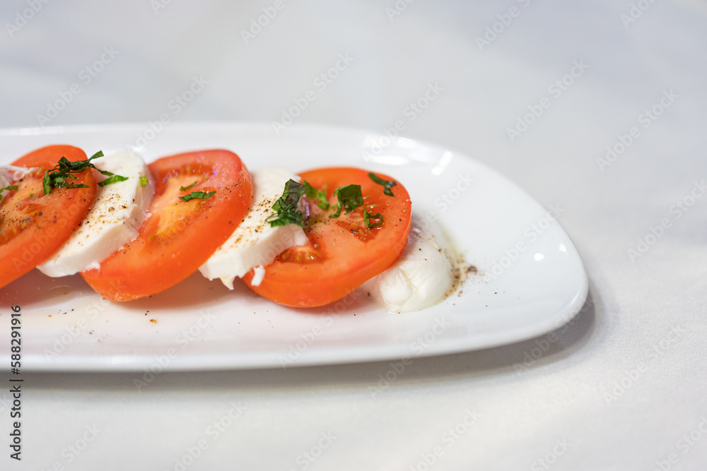 Italian Caprese Salad with Mozzarella cheese, tomatoes, basil, olive oil on white plate at Italian diner, restaurant. Fresh Caprese is traditional Italian food from Italy. Traditional food concept. Italian Caprese Salad with Mozzarella cheese, tomatoes, basil, olive oil on white plate at Italian diner, restaurant. Fresh Caprese is traditional Italian food from Italy. Traditional food concept.