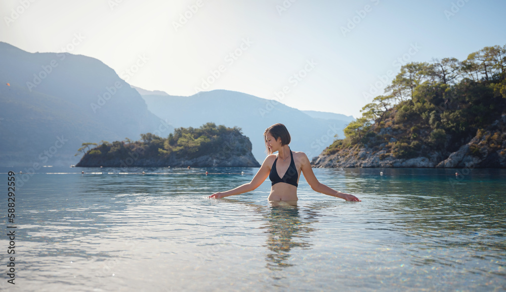 Summer lifestyle portrait of Happy traveller woman in black swimsuit enjoys her tropical beach vacation in Oludeniz Blue Lagoon Turkey.