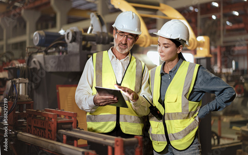 Senior manager train female technician to work in metalwork production factory. Industrial engineer man and woman standing in manufacturing facility talking machinery technology in heavy industry.