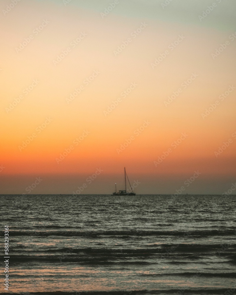 Seascape view at sunset with a boat flowing in, golden cloudy sky background