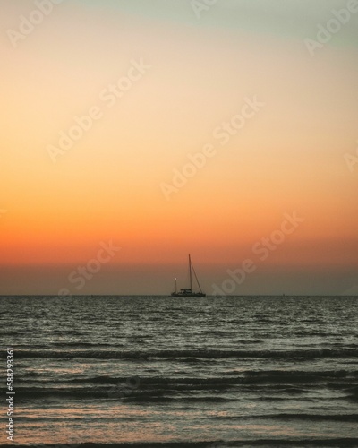 Seascape view at sunset with a boat flowing in, golden cloudy sky background