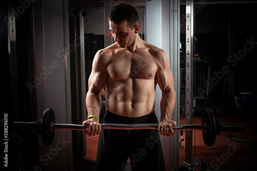 Strong man - bodybuilder with dumbbells in gym, exercising with a barbell