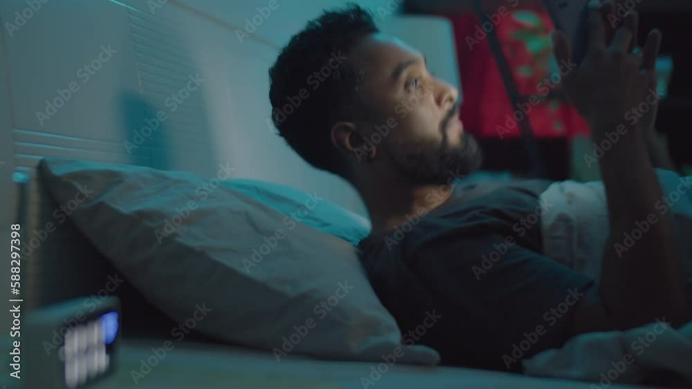 Young bearded man using mobile phone in bed, then lying under blanket and sleeping at night Young bearded man using mobile phone in bed, then lying under blanket and sleeping at night