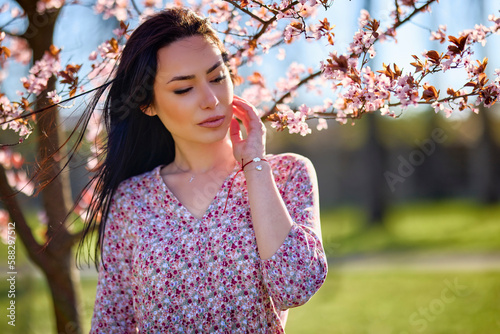 beautiful woman posing by a blooming tree on a sunny spring day.