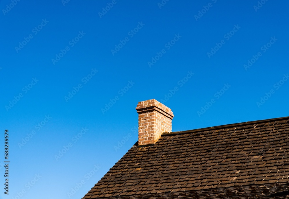 Low-angle closeup of a brick roof with a chimney in the blue sky background