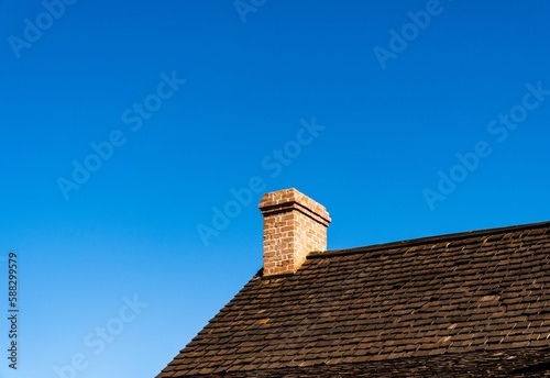 Low-angle closeup of a brick roof with a chimney in the blue sky background