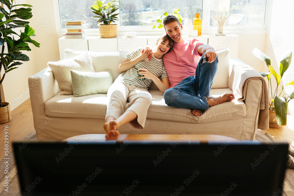 Happy couple watching TV sitting on sofa at home Happy couple watching TV sitting on sofa at home