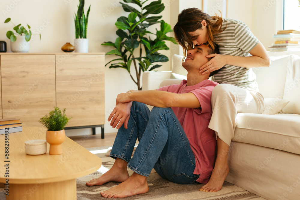 Woman kissing on boyfriend's forehead in living room Woman kissing on boyfriend's forehead in living room