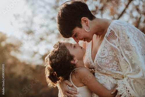 Happy woman rubbing nose with daughter at sunset