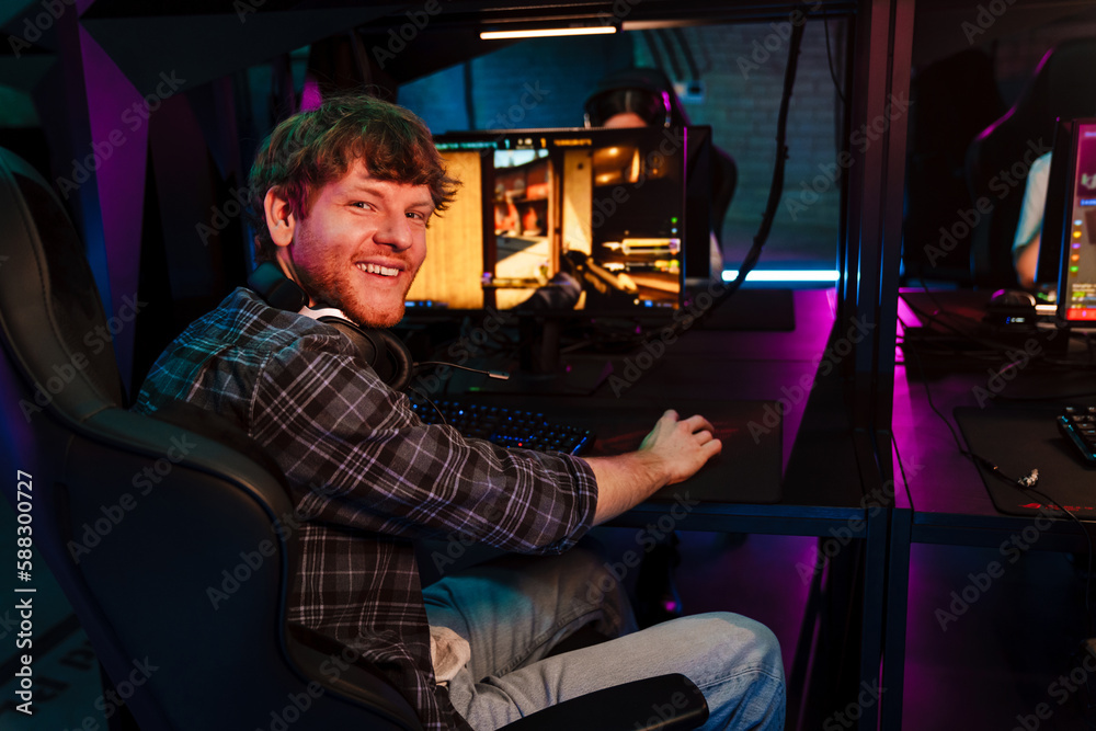 Cheefrul man smiling at camera while playing video game in cybersport club