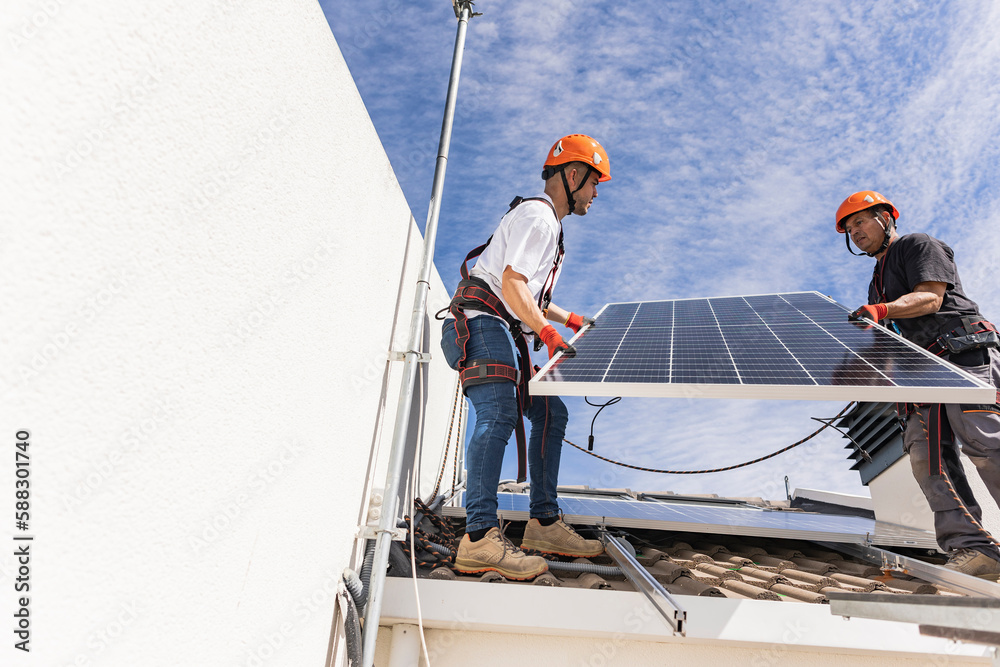 Young technician with colleague installing solar panels on roof Young technician with colleague installing solar panels on roof