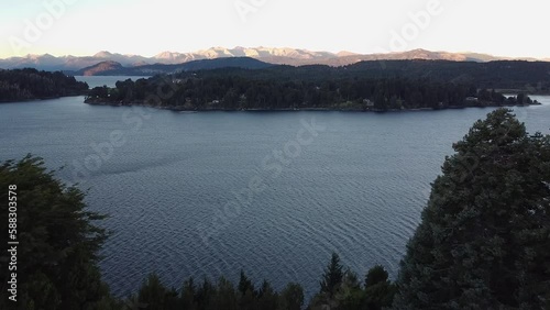 Aerial cinematic shot flying close the trees revealing the lake Nahuel Huapi at Sunset with Andes Mountain Range in the bacground the Patagonia Argentina. photo