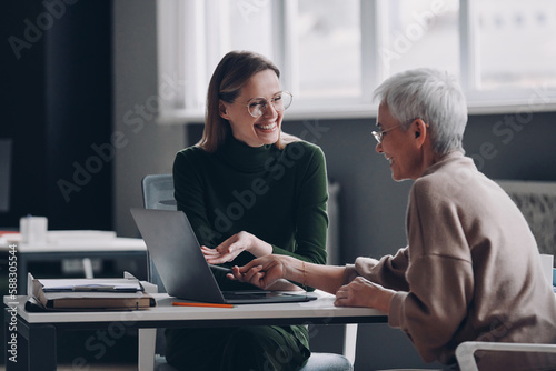 Happy financial advisor pointing laptop while discussing options with senior woman in office photo