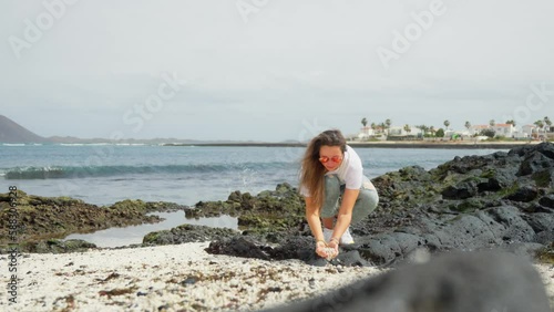 A girl in white on a volcanic beach touches pebbles. photo