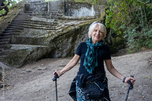 Smiling senior woman standing with walking sticks at Etruscan Pyramid of Bomarzo photo