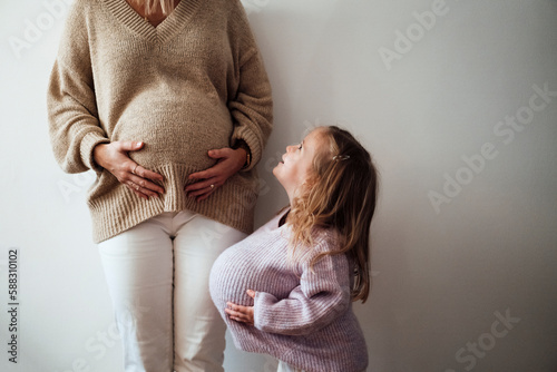 Daughter imitating mother's pregnancy in front of wall