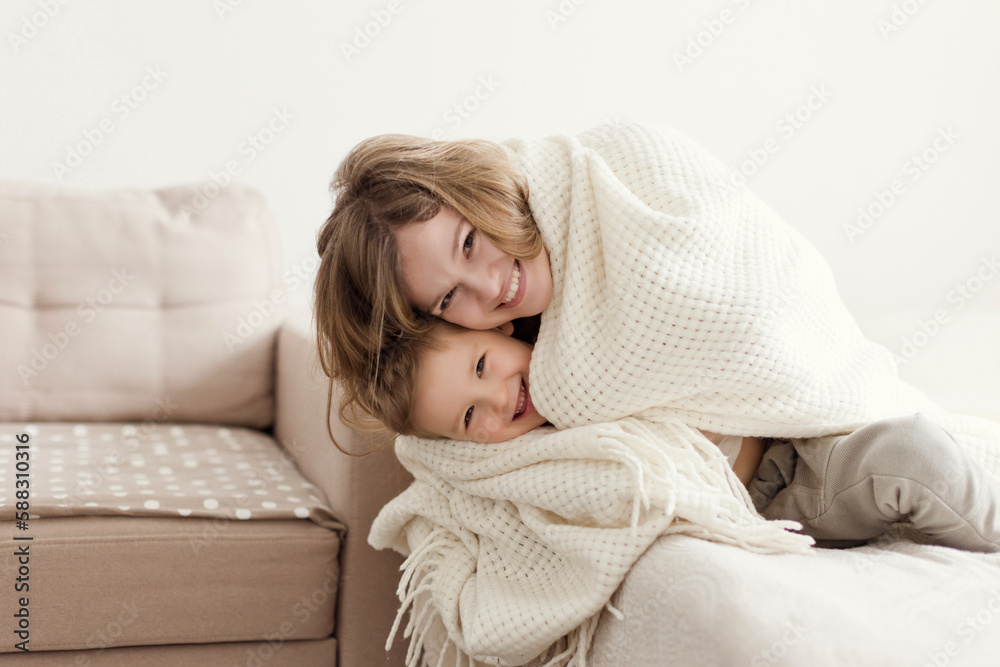 Happy mother and son wrapped in blanket on sofa at home