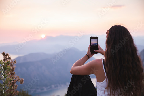 Young woman photographing sunset through smart phone