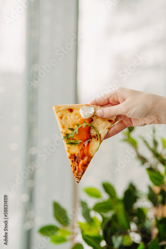 A piece of pizza in his hand, against the backdrop of the restaurant, Side view of the pizza. The concept of Italian cuisine, street food, fast food, fast food. Banner