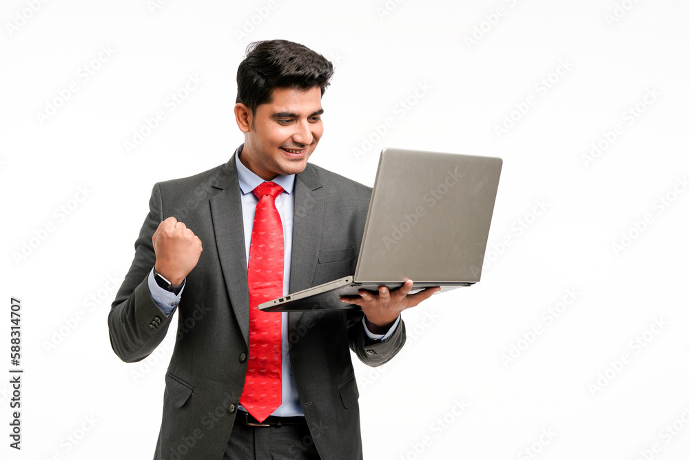 Young indian businessman in suit, holding laptop and giving a winning expression. Young indian businessman in suit, holding laptop and giving a winning expression.