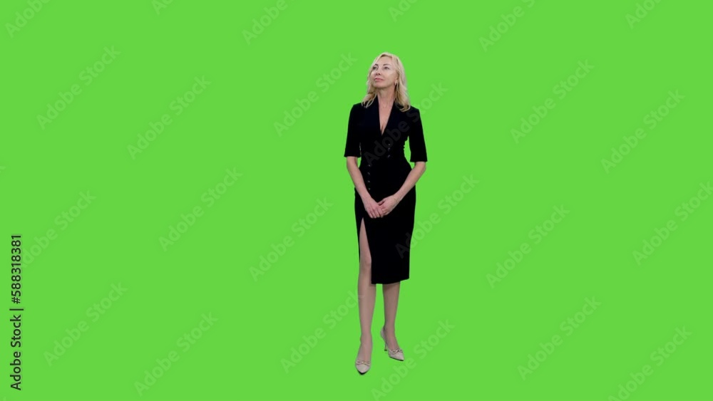 Slender middle aged blond woman in black dress standing and something watching on green background, Chroma key, 4k pre-keyed footage Slender middle aged blond woman in black dress standing and something watching on green background, Chroma key, 4k pre-keyed footage