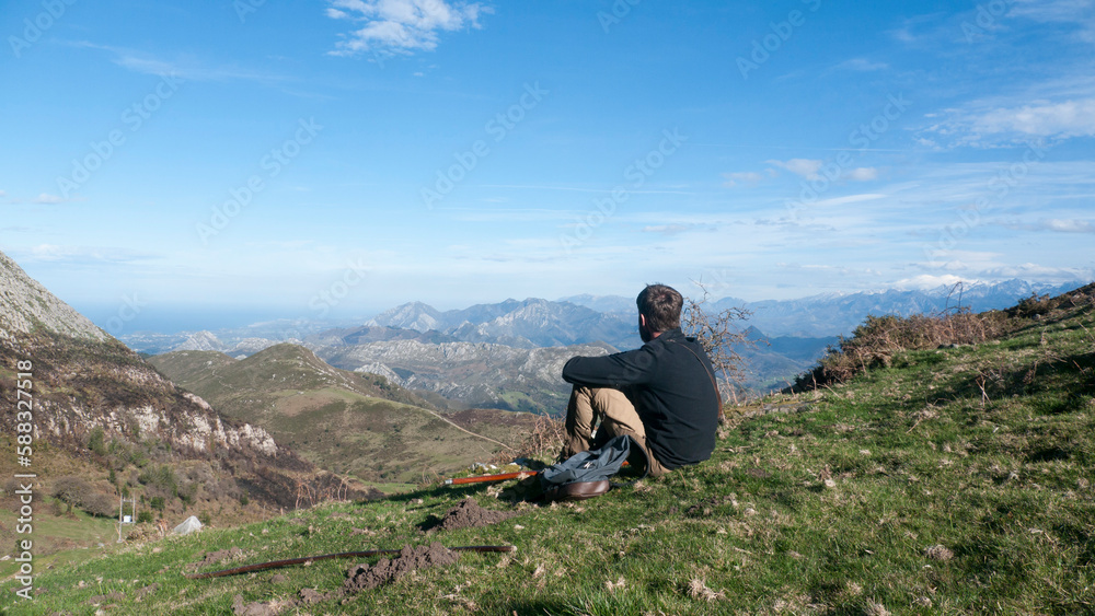 Hombre joven barbudo sentado  en ladera de montaña de Asturias