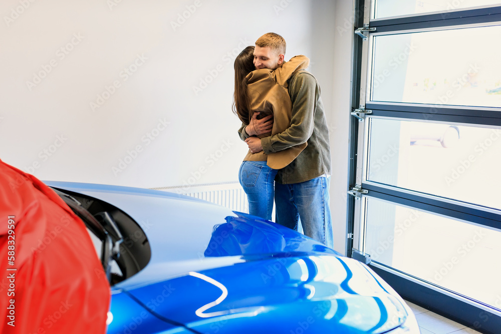 A young couple is happy about buying a new car. The car is covered with a red cloth. Emotional people A young couple is happy about buying a new car. The car is covered with a red cloth. Emotional people